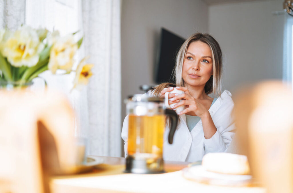 Frau mit Teetasse am Frühstückstisch, Symbol für Ruhe und Selbstfürsorge bei Endometriose